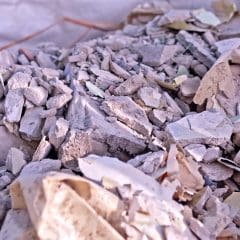 A close-up view of a pile of rubble made up of broken plaster, debris, and fragments of drywall or concrete, with bits of paper and small pieces scattered throughout.
